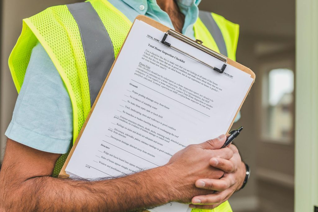 Construction worker in a neon-yellow safety vest holding a clipboard with a printed inspection checklist.